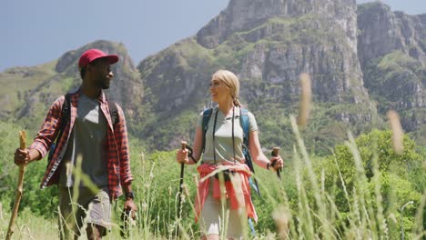 Happy-diverse-couple-hiking-with-backpacks-in-mountains,-slow-motion