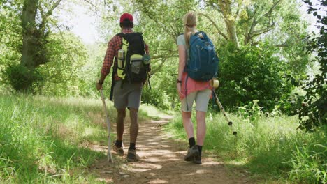 Diverse-couple-hiking-with-backpacks-in-park-on-sunny-day,-slow-motion