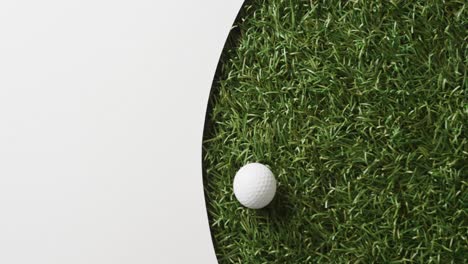 Close-up-of-golf-ball-on-grass-with-white-background,-copy-space,-slow-motion