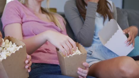 Diverse-teenager-girls-friends-eating-popcorn-and-watching-tv-at-home,-slow-motion
