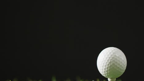 Close-up-of-golf-tee-and-ball-on-grass-and-black-background,-copy-space,-slow-motion