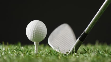 Close-up-of-golf-club-and-ball-on-grass-and-black-background,-copy-space,-slow-motion