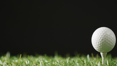 Close-up-of-golf-tee-and-ball-on-grass-and-black-background,-copy-space,-slow-motion