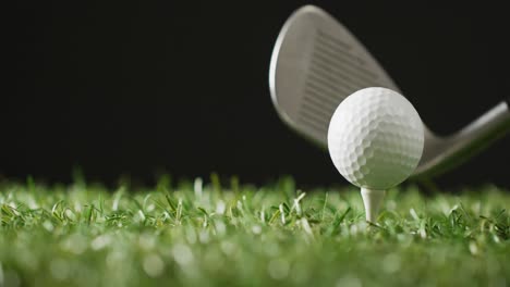 Close-up-of-golf-club-and-ball-on-grass-and-black-background,-copy-space,-slow-motion