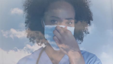 Animation-of-sky-with-clouds-over-african-american-female-doctor-wearing-face-mask