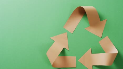Close-up-of-recycling-symbol-of-paper-arrows-on-green-background,-with-copy-space