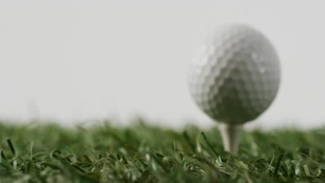 Close-up-of-golf-tee-and-ball-on-grass-and-white-background,-copy-space,-slow-motion