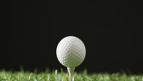 Nahaufnahme-Von-Golf-Tee-Und-Ball-Auf-Gras-Und-Schwarzem-Hintergrund,-Kopierraum,-Zeitlupe