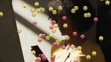 Animation-Von-Social-Media-Emoji-Symbolen-über-Einer-Afroamerikanischen-Frau,-Die-Ihr-Smartphone-Nutzt