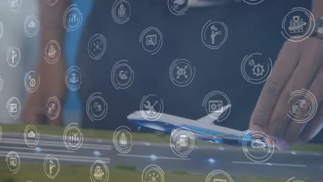 Animation-of-digital-icons-over-mid-section-of-a-woman-flying-a-airplane-model-at-office