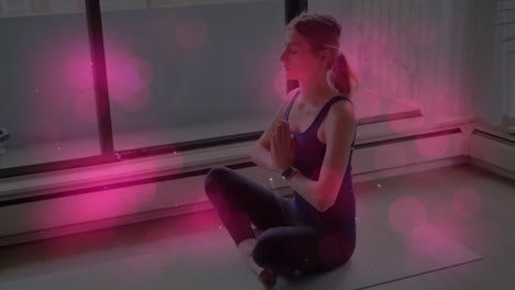 Animation-of-pink-glowing-spots-over-caucasian-fit-woman-practicing-yoga-at-home
