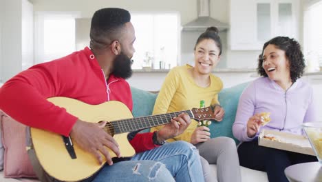 Happy,-diverse-female-and-male-friends-playing-guitar-and-listening-at-home-in-slow-motion