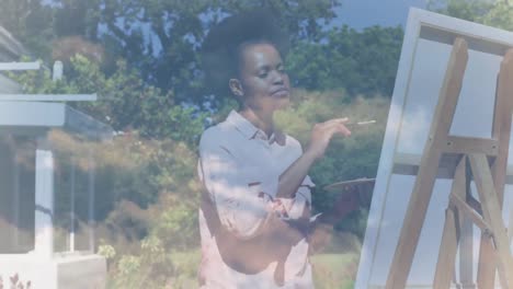 Animation-of-clouds-over-african-american-woman-painting-on-easel-in-garden