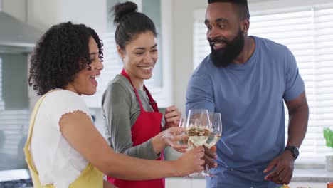 Happy-diverse-female-and-male-friends-drinking-wine-and-cooking-in-kitchen,-in-slow-motion