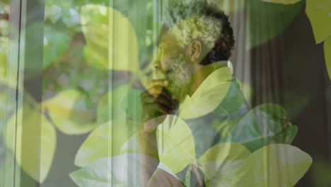 Animation-of-leaves-over-african-american-man-looking-through-window,-slow-motion