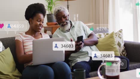 Animation-of-social-media-icons-and-numbers-over-african-american-man-and-woman-with-laptop