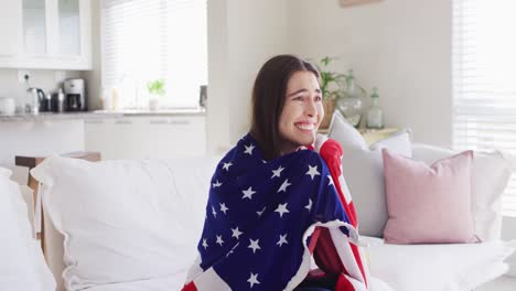 Happy-caucasian-woman-sitting-on-couch-with-flag-of-usa-and-watching-tv-in-living-room