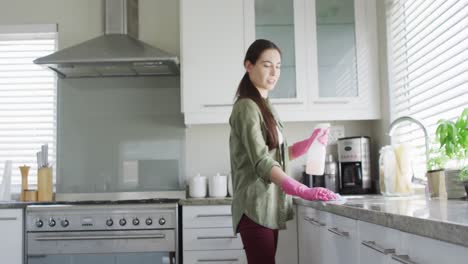 Caucasian-woman-wearing-rubber-gloves-and-cleaning-table-in-kitchen