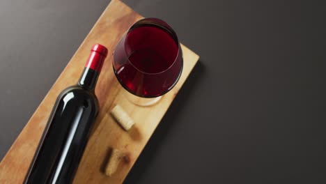 Red-wine-glass,-bottle-and-cork-lying-on-wooden-board-with-copy-space-on-black-background
