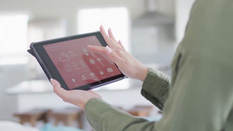 Caucasian-woman-using-tablet-with-smart-home-interface-on-screen-at-home