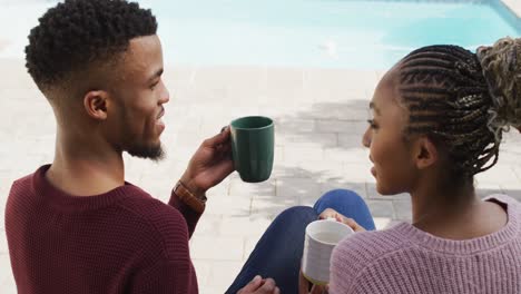 Happy-african-american-couple-embracing-and-relaxing-with-coffee-outside-house