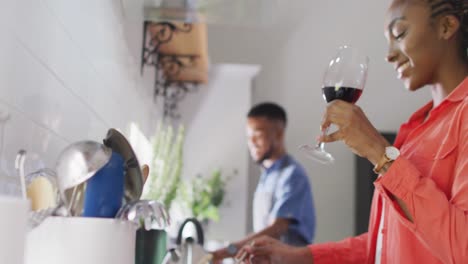 Happy-african-american-couple-preparing-meal-in-kitchen-and-drinking-wine