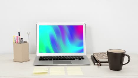 Animation-of-laptop-with-colorful-moving-shapes-on-screen-on-desk