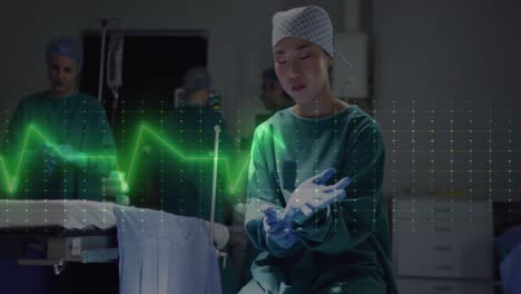 Animation-of-cardiograph-over-asian-female-surgeon-wearing-medical-gloves-at-hospital