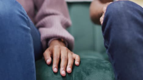 Hands-of-african-american-couple-sitting-on-sofa-and-touching