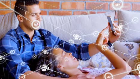 Animation-of-network-of-digital-icons-over-biracial-couple-using-smartphone-together-at-home