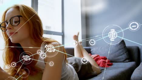 Animation-of-network-of-icons-over-caucasian-woman-using-digital-tablet-lying-on-couch-at-home