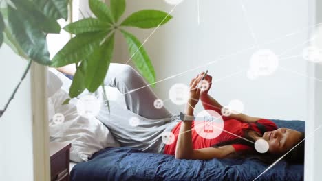 Animation-of-network-of-digital-icons-over-asian-woman-using-smartphone-lying-on-the-bed-at-home