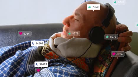 Animation-of-social-media-icons-over-caucasian-man-wearing-headphone-lying-on-the-couch-at-home