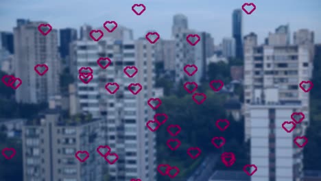 Animation-of-multiple-red-heart-icons-floating-against-aerial-view-of-tall-buildings