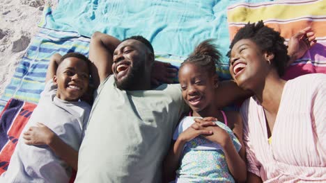 Video-of-happy-african-american-family-lying-on-beach-and-laughing