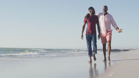 Video-Eines-Glücklichen-Afroamerikanischen-Seniorvaters-Und-Eines-Erwachsenen-Sohnes,-Die-Am-Strand-Spazieren-Gehen