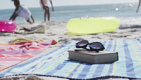 Video-of-sunglasses,-book,-towels-and-beach-equipment-lying-on-beach