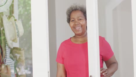 Sonriente-Mujer-Mayor-Afroamericana-Abriendo-La-Puerta-Para-Recibir-Al-Visitante,-Cámara-Lenta