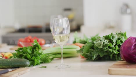 Glasses-of-white-wine-and-fresh-vegetables-on-kitchen-counter-top,-slow-motion