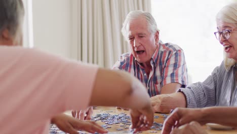 Diverse-group-of-happy-senior-male-and-female-friends-doing-jigsaw-in-living-room,-slow-motion