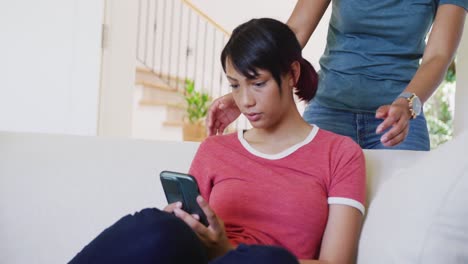 Happy-biracial-sisters-sitting-on-sofa-and-using-smartphone,-in-slow-motion