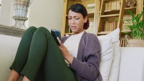 Sad-biracial-teenager-girl-sitting-on-sofa,-using-smartphone-and-crying,-in-slow-motion