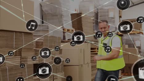 Animation-of-network-of-digital-icons-against-caucasian-male-worker-stacking-boxes-at-warehouse