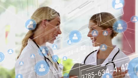 Animation-of-network-of-profile-icons-over-two-caucasian-female-doctors-discussing-at-hospital