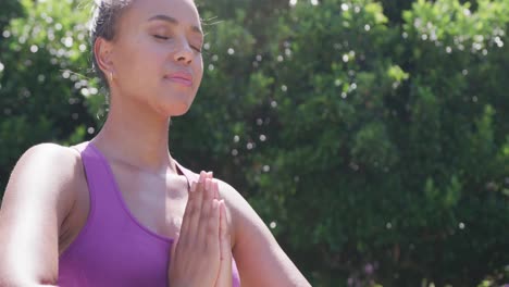 Happy-biracial-woman-doing-yoga-and-meditating-in-garden,-in-slow-motion