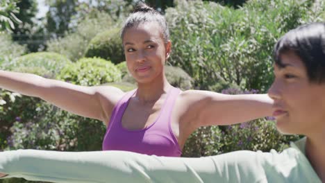 Happy-biracial-sisters-doing-yoga-and-stretching-in-garden,-in-slow-motion
