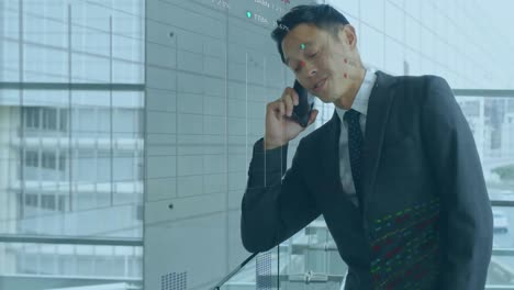 Animation-of-stock-market-data-processing-over-asian-businessman-talking-on-smartphone-at-office