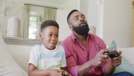 Happy-african-american-father-and-son-watching-playing-video-games-together,-in-slow-motion