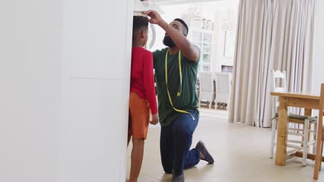 Happy-african-american-father-and-son-measuring-height,-in-slow-motion