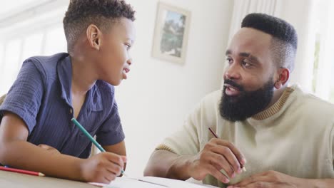 Glücklicher-Afroamerikanischer-Vater-Und-Sohn-Sitzen-Am-Tisch-Und-Machen-Gemeinsam-Hausaufgaben,-In-Zeitlupe